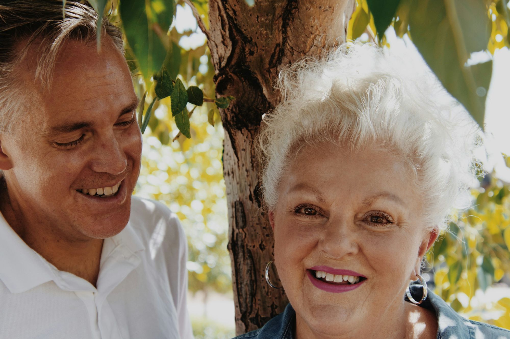 A man and an older woman smiling together under a tree