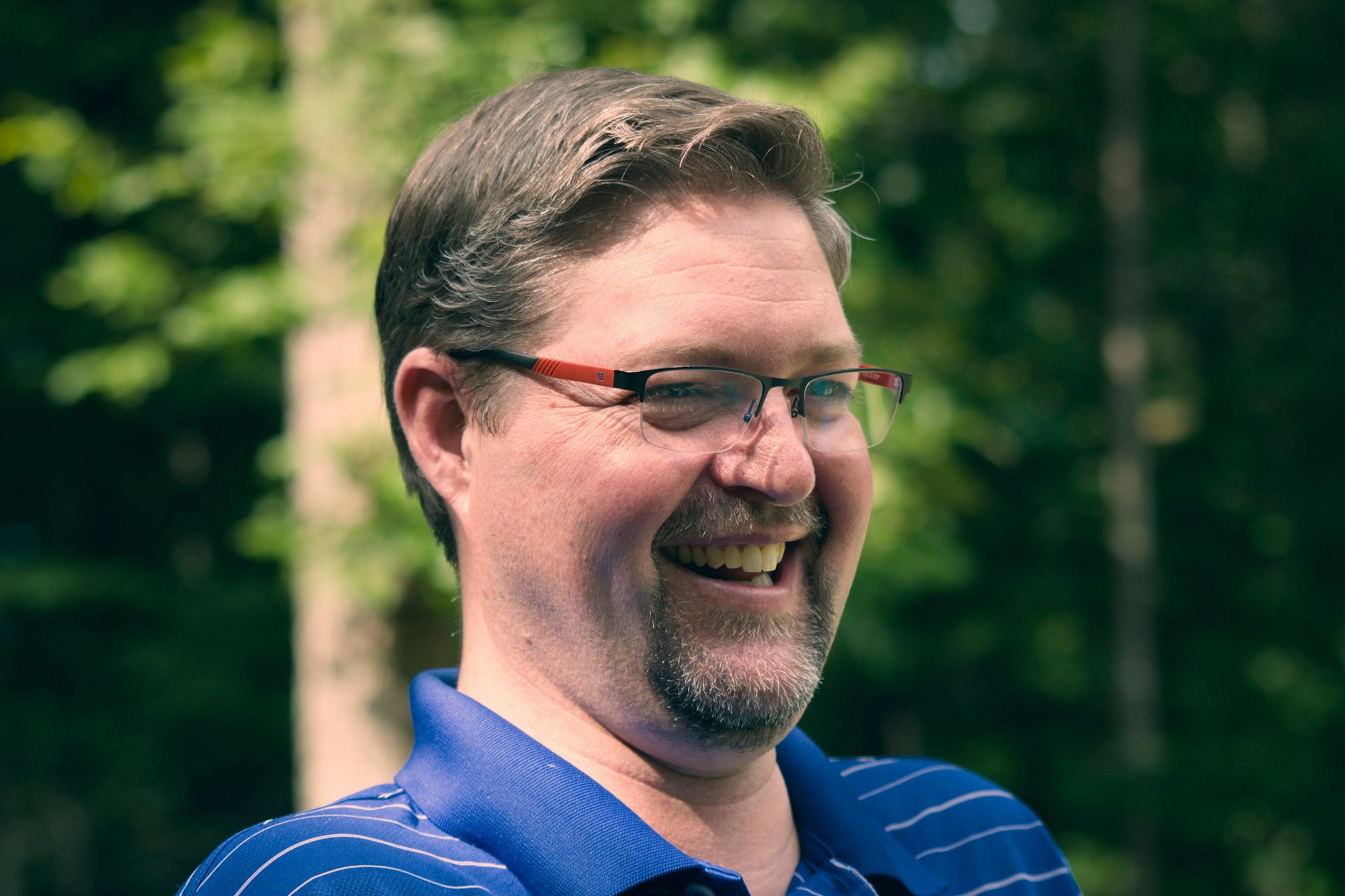 A man in glasses laughing outdoors